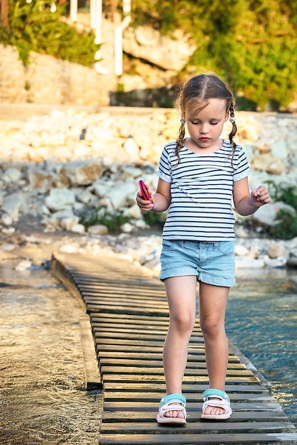 a little girl carefully crosses a mountain river on a makeshift wooden bridge