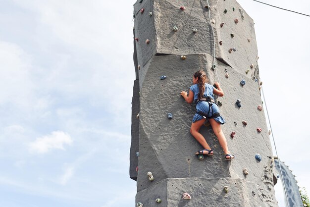 Photo little girl in casual blue clothes training rock climbing outdoors