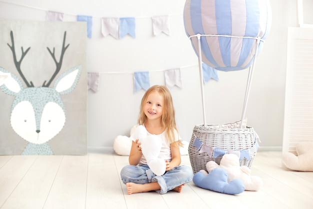 A little girl in casual clothes holds a cloud pillow against the wall of a decorative balloon. The child plays in the children's room. The concept of childhood. birthday, holiday decorations