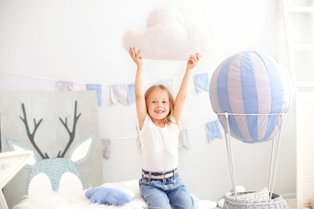 A little girl in casual clothes holds a cloud pillow