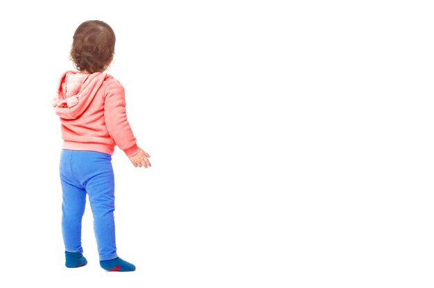 A little girl in casual clothes stands with her back on a white background.