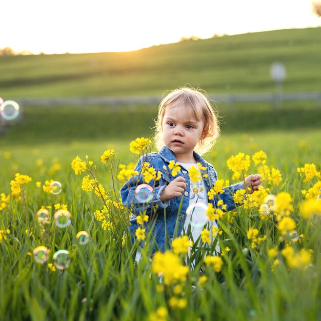 Маленькая девочка ловит мыльные пузыри на цветущем лугу