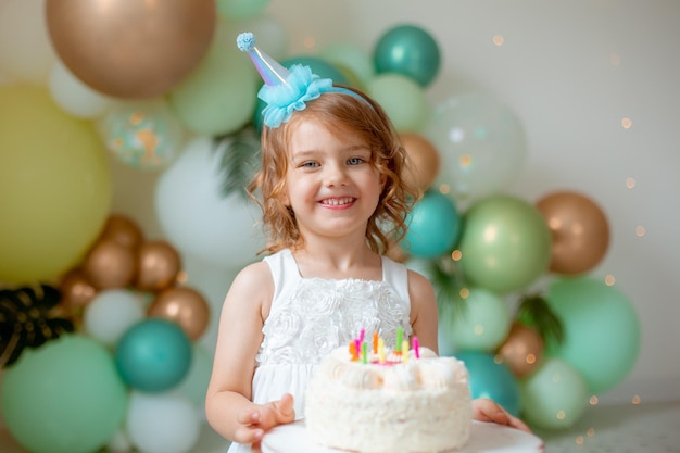Little girl celebrates her birthday against the background of balloons blowing out candles