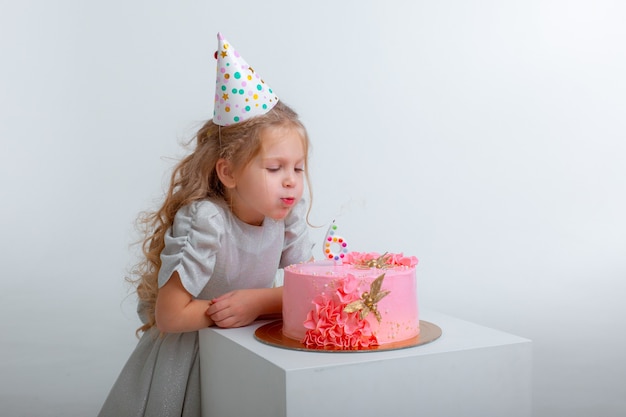 小さな女の子はケーキの上のろうそくを吹き消す彼女の誕生日を祝います