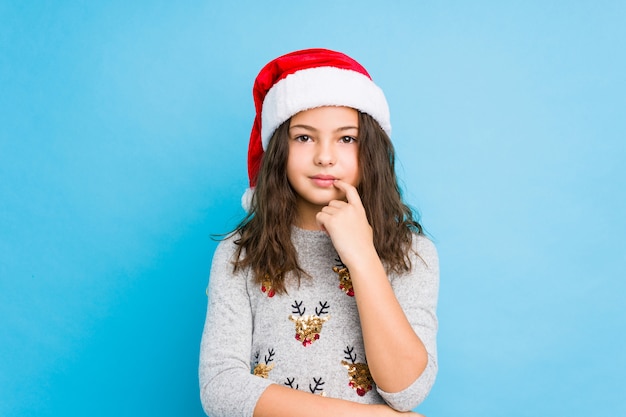 Little girl celebrating christmas day looking sideways with doubtful and skeptical expression.