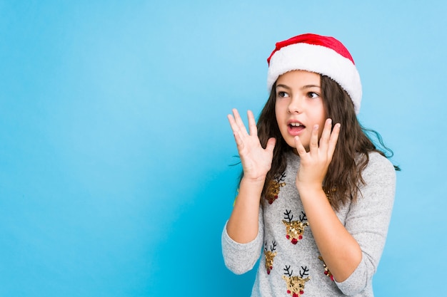 Little girl celebrating christmas day shouts loud, keeps eyes opened and hands tense.