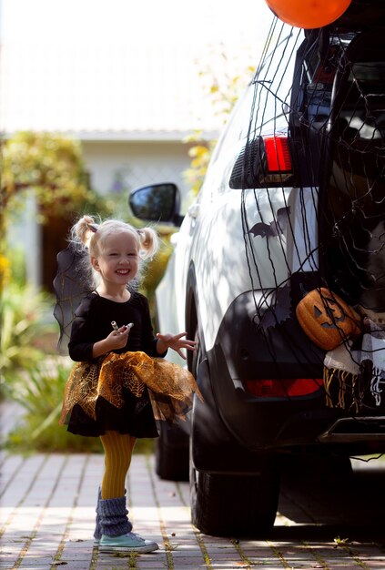 ハロウィーンの車のトランクを祝う少女は、秋の休日に家にいる