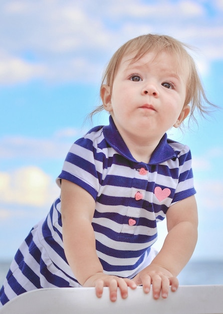 Little girl chaise longue striped dress against sky