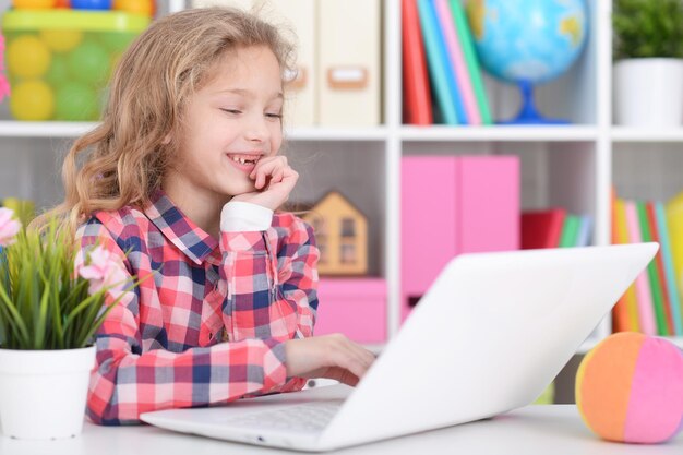 Little girl in checkered shirt using modern laptop in her room