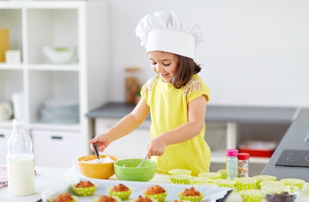 Photo little girl in chefs toque baking muffins at home