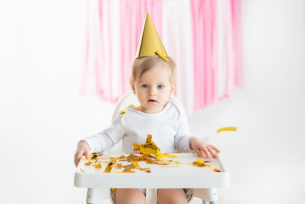 Little girl child cheerfully throws up colorful tinsel and confetti on a gray blue background. Holiday. Happy excited laughing baby on birthday.