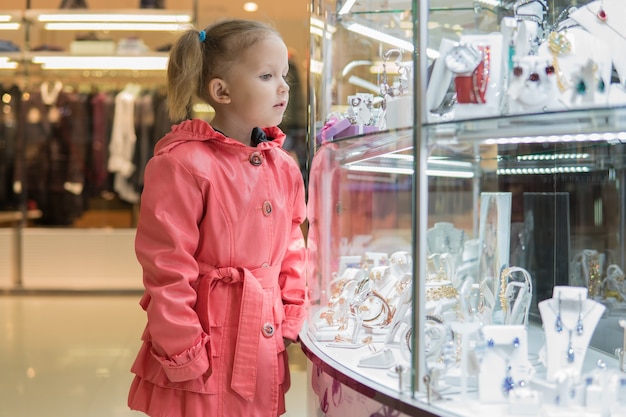 La bambina esamina le vetrine dei negozi in un centro commerciale