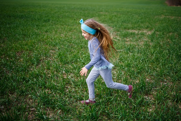 Little girl child runs on green grass in the field, sunny spring weather, smile and joy of the child, blue sky with clouds