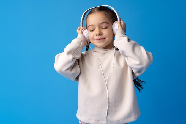 Little girl child wear headphones listen to music over blue background