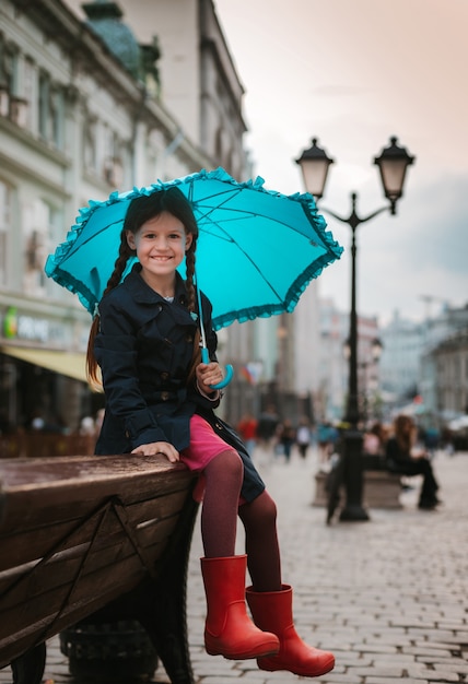 Little girl  child with an umbrella in rubber boots having fun on a bench in the center of Moscow