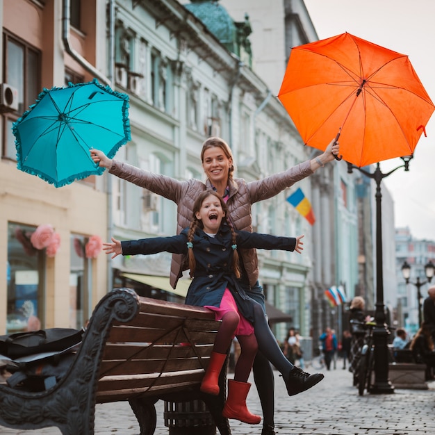 Little girl  child with an umbrella in rubber boots having fun with her mother on a bench in the center of Moscow