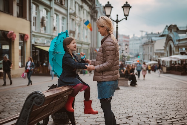 Little girl child with umbrella and rubber boots having fun with her mother