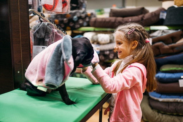 Foto la bambina sceglie i vestiti per il cucciolo nel negozio di animali. cliente bambino che acquista cani in generale in negozio di animali, prodotti per animali domestici