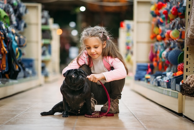 小さな女の子がペットショップで子犬の家を選ぶ