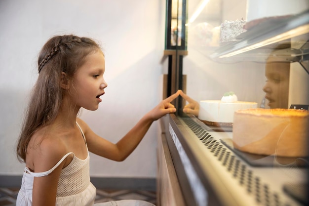Маленькая девочка выбирает сладости в витрине магазина