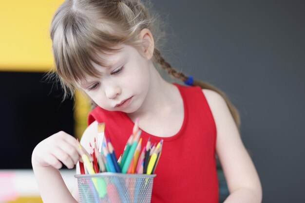 Little girl choosing multicolored pencils from glass fine art lessons for children concept