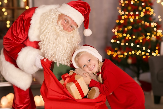 Маленькая девочка выбирает подарок из подарочного пакета Санта-Клауса в украшенной комнате