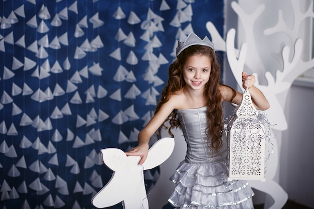 Маленькая девочка в рождественских украшениях. Портрет красивой маленькой девочки с длинными вьющимися волосами с короной