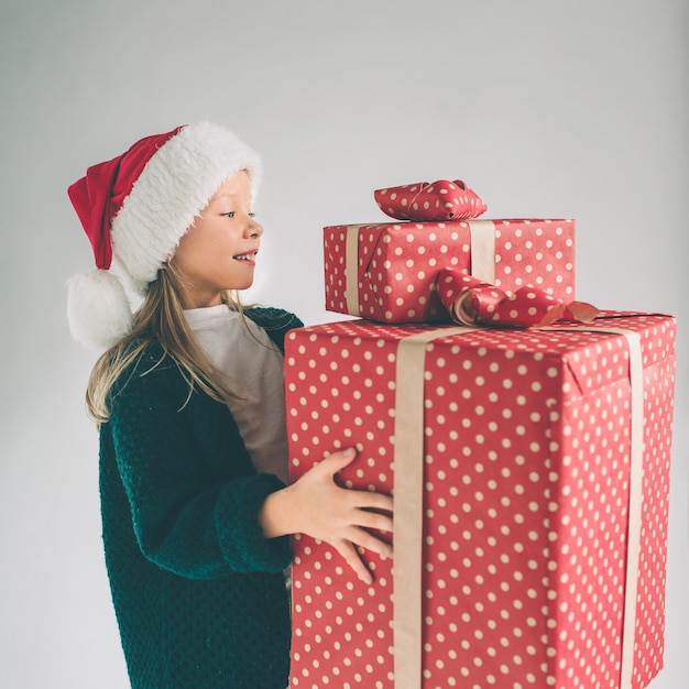 Little girl in a Christmas hat holding gifts on white background