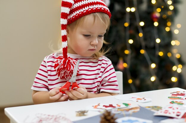 Little girl in Christmas hat making decorations for Christmas Kids creativity and Christmas craft