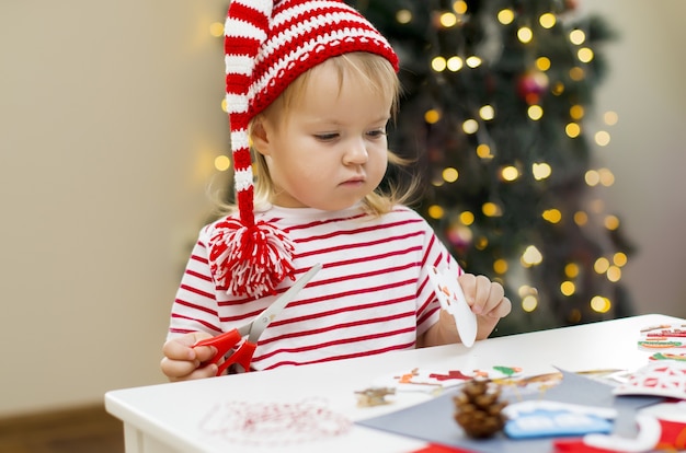 Little girl in Christmas hat making decorations for Christmas Kids creativity and Christmas craft