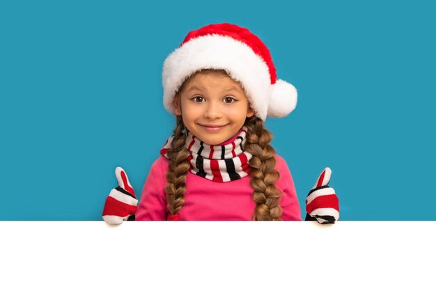 Little girl in a Christmas hat on a white wall.