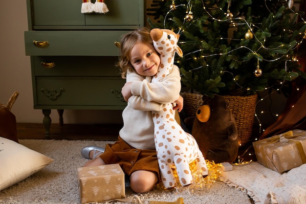 Bambina nella casa di natale e che abbraccia la sua giraffa giocattolo carino