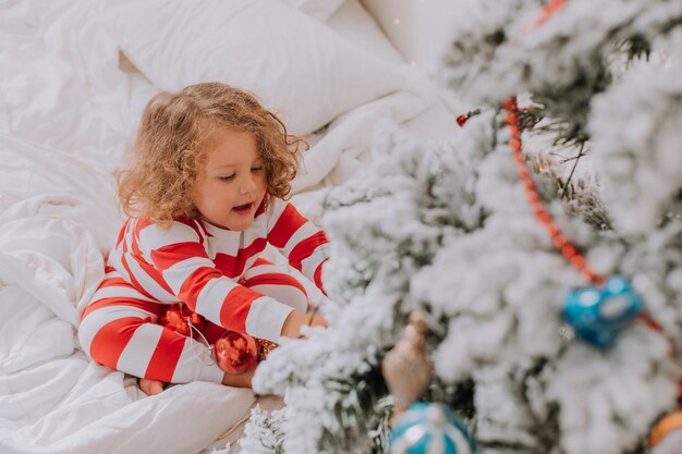 クリスマスの縞模様のパジャマの少女がクリスマスツリーを飾ります。ライフスタイル。高品質の写真