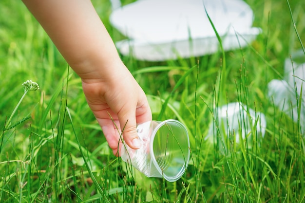 Little girl cleans plastic utensils on the green grass in the park