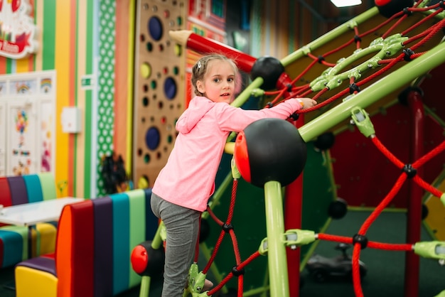 Little girl climbing on a ropes on playground in childrens entertainment center. Child sport activity. Happy childhood