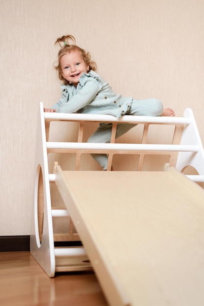 The little girl climbs up a wooden plate in the gym