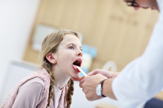 喉頭学者によって検査されているクリニックの少女