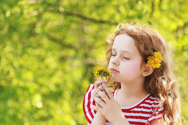 Little girl closed her eyes and breathes yellow dandelions in the field.