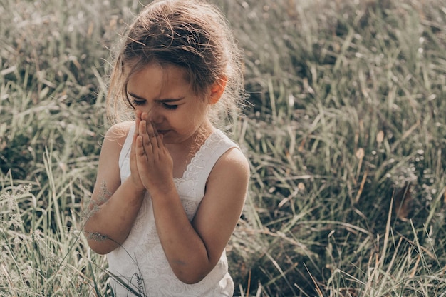 Little girl closed her eyes praying outdoors Hands folded in prayer concept for faith spirituality and religion Peace hope dreams concept