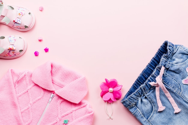 La raccolta dei vestiti della bambina piana giaceva con t-shirt floreale, jeans, sandali su sfondo rosa.