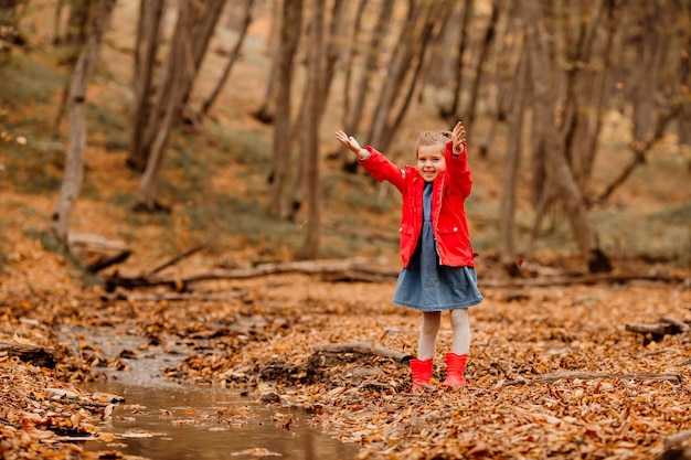 A little girl in a coat and red rubber boots walking in the autumn forest. High quality photo