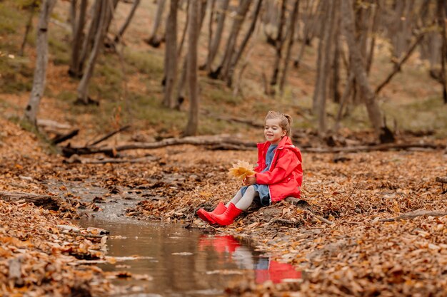 A little girl in a coat and red rubber boots walking in the autumn forest. High quality photo