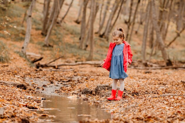 秋の森を歩いているコートと赤いゴム長靴の少女。高品質の写真