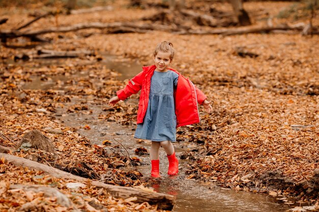 秋の森を歩いているコートと赤いゴム長靴の少女。高品質の写真