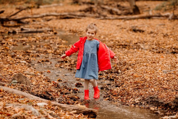 A little girl in a coat and red rubber boots walking in the autumn forest. High quality photo