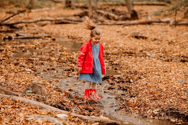 A little girl in a coat and red rubber boots walking in the autumn forest. High quality photo