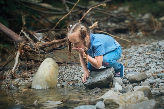 a little girl collects water from a mountain river in her palm and drinks it