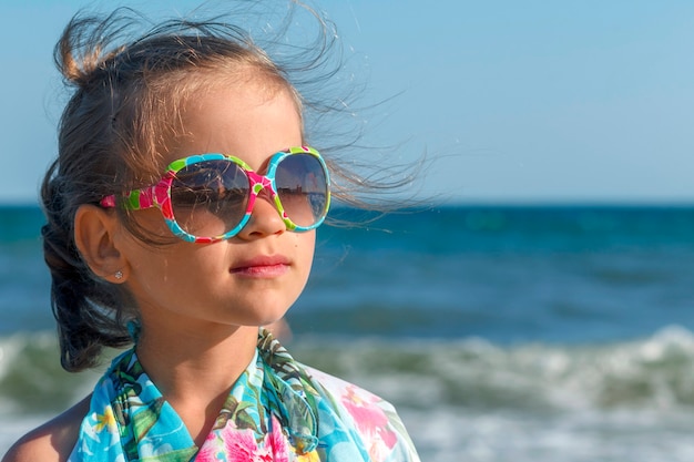 Little girl in colored sunglasses on a background of the sea looks in the distance and dreams of something