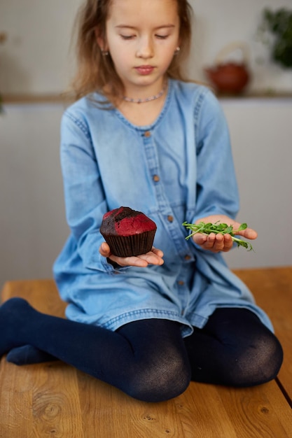 Little girl comparing food choosing microgreen against sweet\
cake healthy dieting habit concept of proper nutrition the right\
choice food