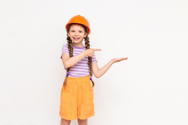 A little girl in a construction helmet holds your advertisement on her hand on a white isolated background The concept of renovation in the children's room